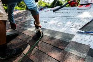 Roofing contractor using a nail gun to install asphalt shingles over roof underlayment