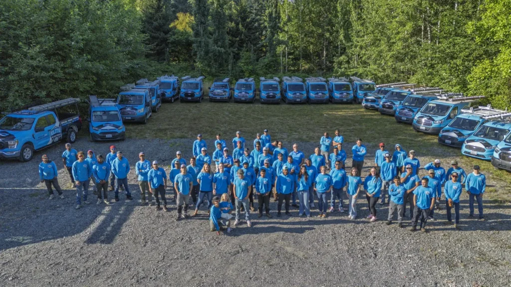 Elite Roofing & Remodel team photo featuring roofing crews and branded service vehicles at company headquarters￼